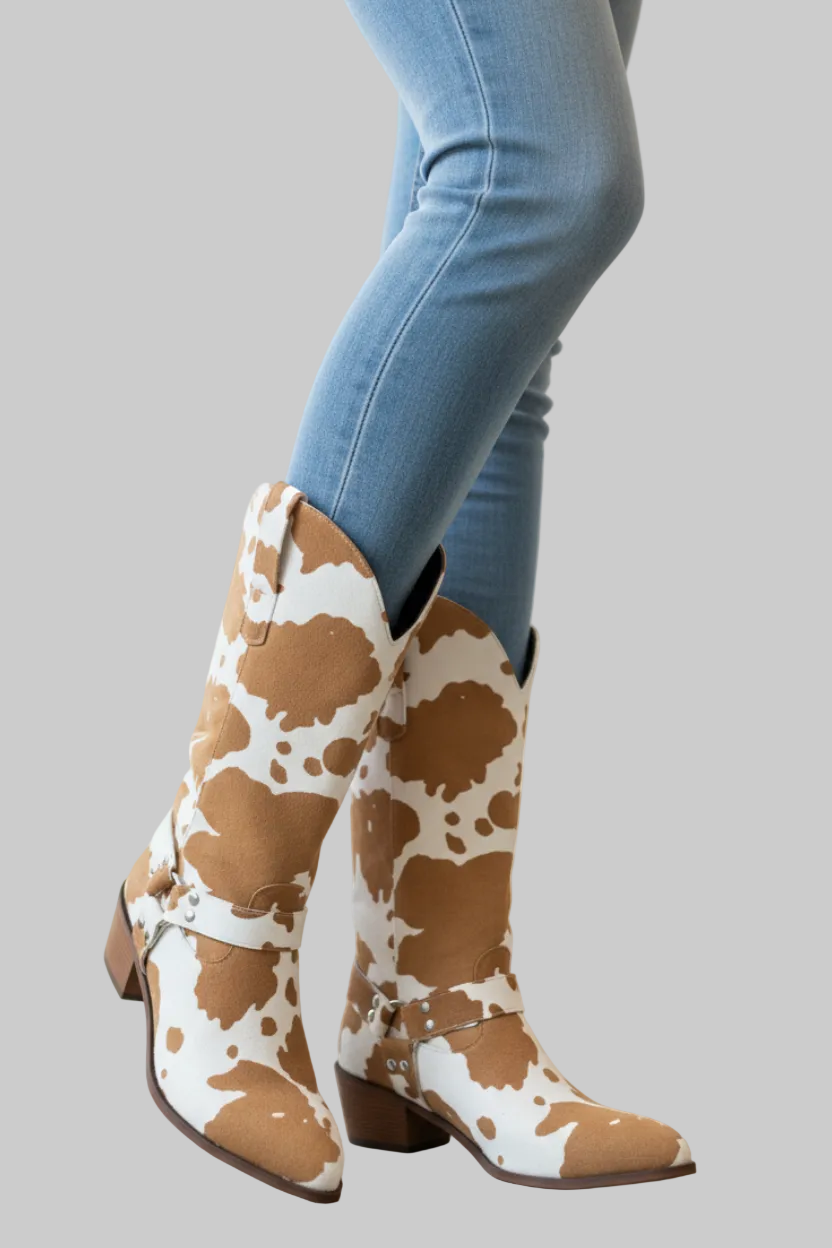 Brown and white cow print faux leather western boots with notched mid-calf shaft, harness strap with silver hardware, pointed toe, and stacked block heel | The Pretty Pistol