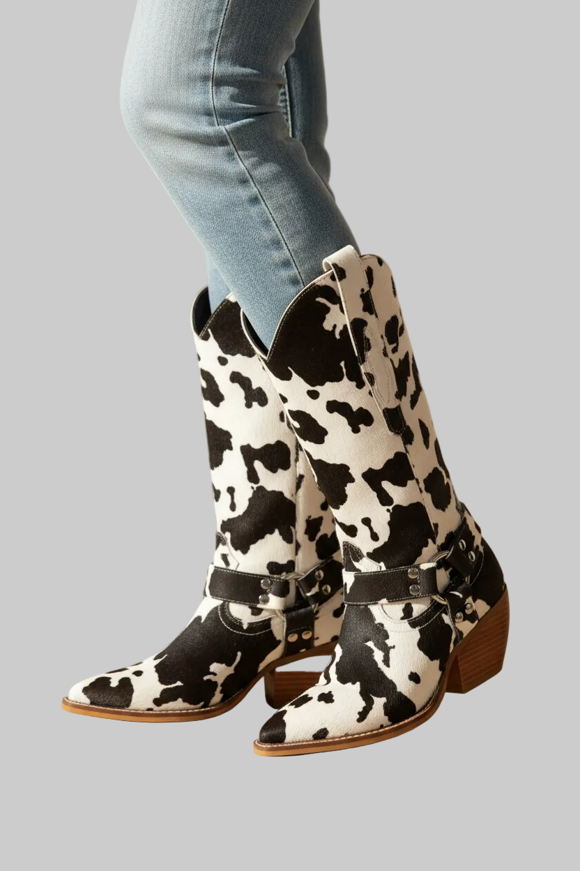 Black and white cow print faux leather western boots with notched mid-calf shaft, harness strap with silver hardware, pointed toe, and stacked block heel | The Pretty Pistol