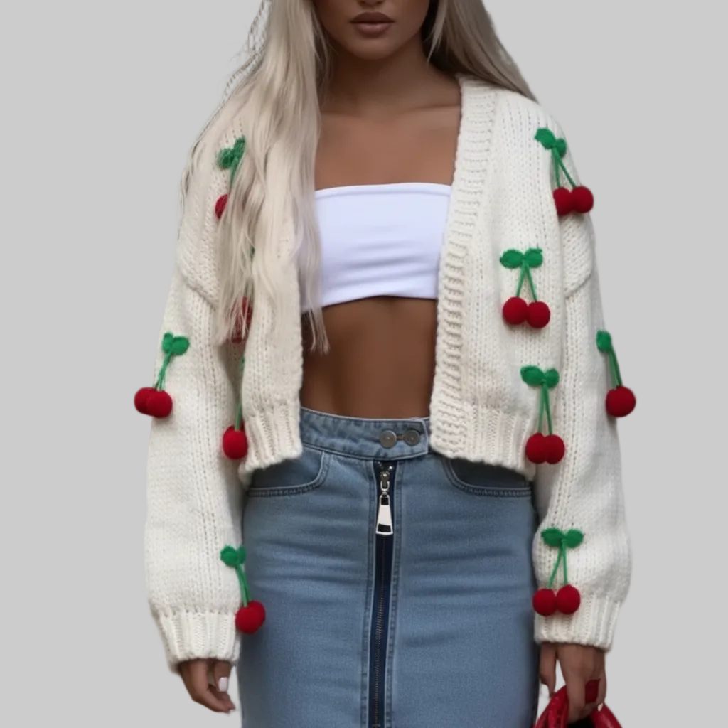 Cream chunky knit open-front cardigan with 3D red cherry appliqués, styled over a white crop top and zip-front denim mini skirt, gray background | The Pretty Pistol